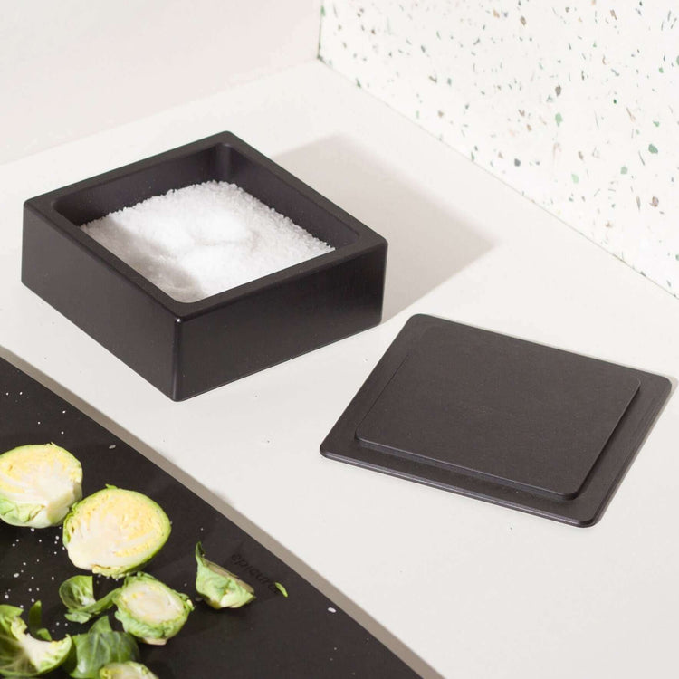 Epicurean Salt Cellar in Slate on a counter filled with salt next to a Slate Epicurean Cutting Board and sliced Brussel Sprouts