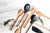 A group shot of various utensils from our lines on a flat counter next to some fresh herbs