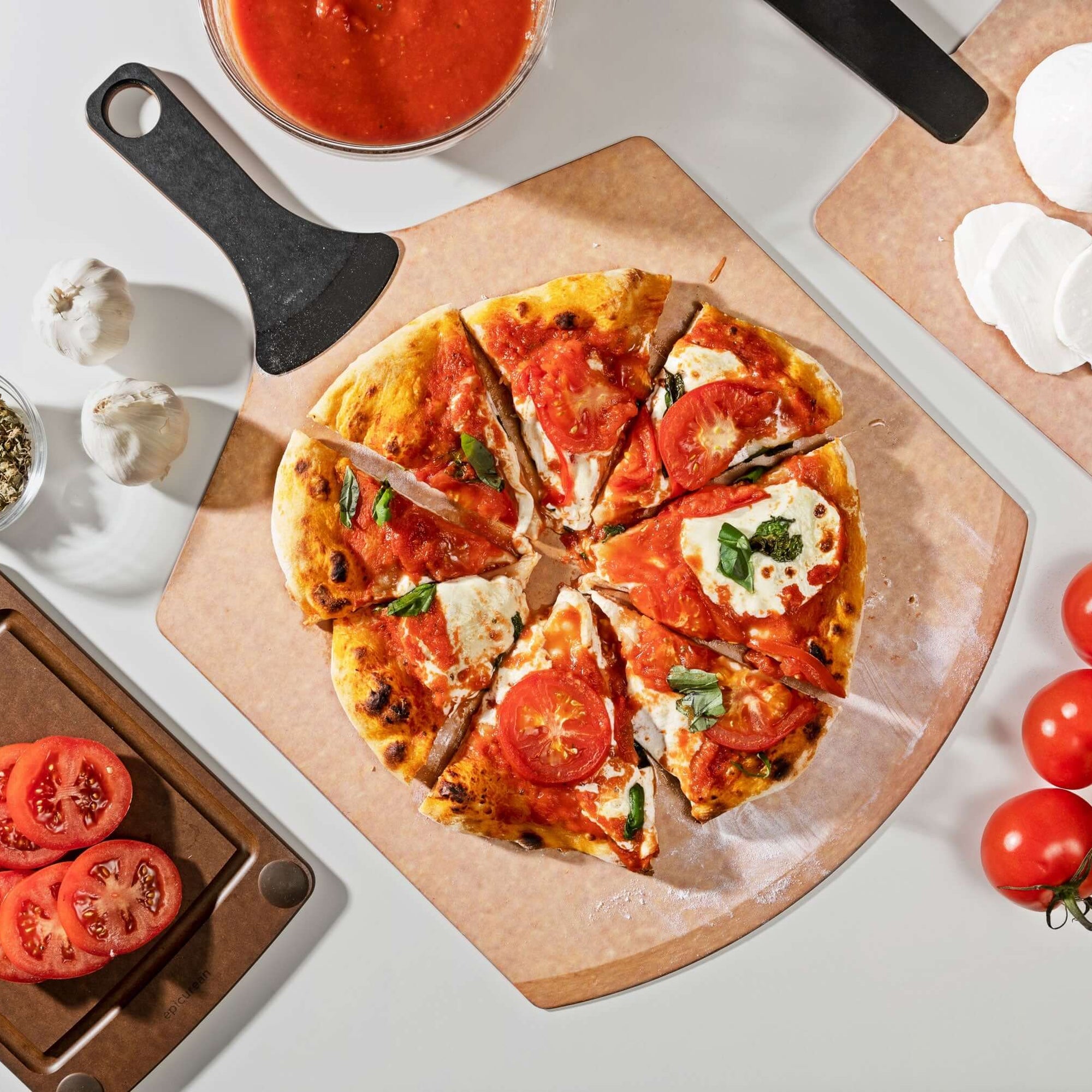 Epicurean Pizza Peel Plus in Natural with a delicious pizza and assorted toppings placed on additional Epicurean boards