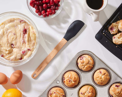 Silicone Series Natural/Black Small Spatula on a white counter with all of the ingredients to bake cranberry muffins and enjoy a cup of coffee