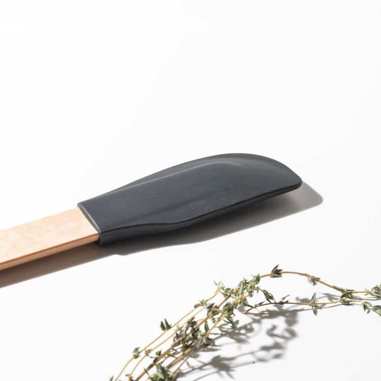 Close up of the Silicone Series Small Spatula on a white background with herbs