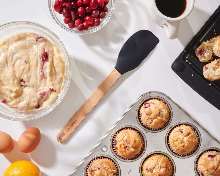 Silicone Series Natural/Black Large Spatula on a white counter with all of the ingredients to bake cranberry muffins and enjoy a cup of coffee