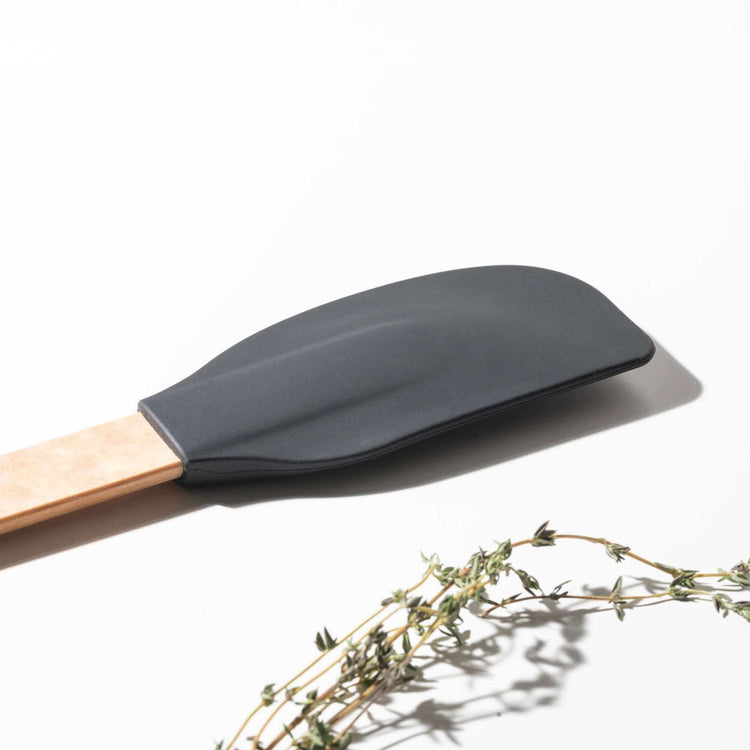 Close up of the Silicone Series Large Spatula on a white background with herbs