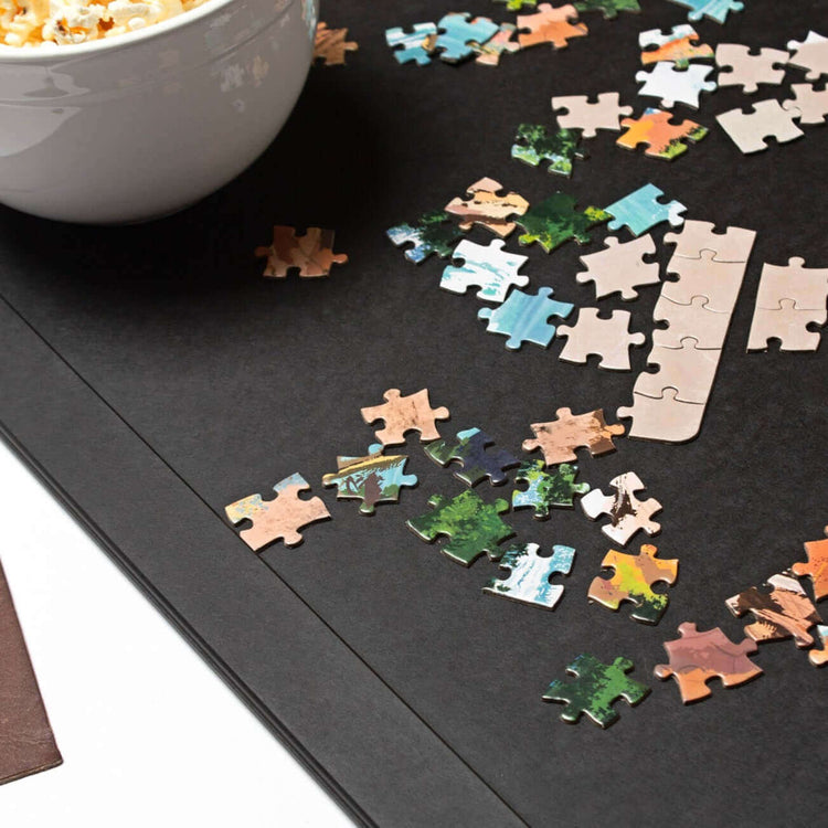 Epicurean Board Game Board in Large Slate Ready For Game Night with colorful assorted puzzle pieces and a bowl of freshly popped popcorn