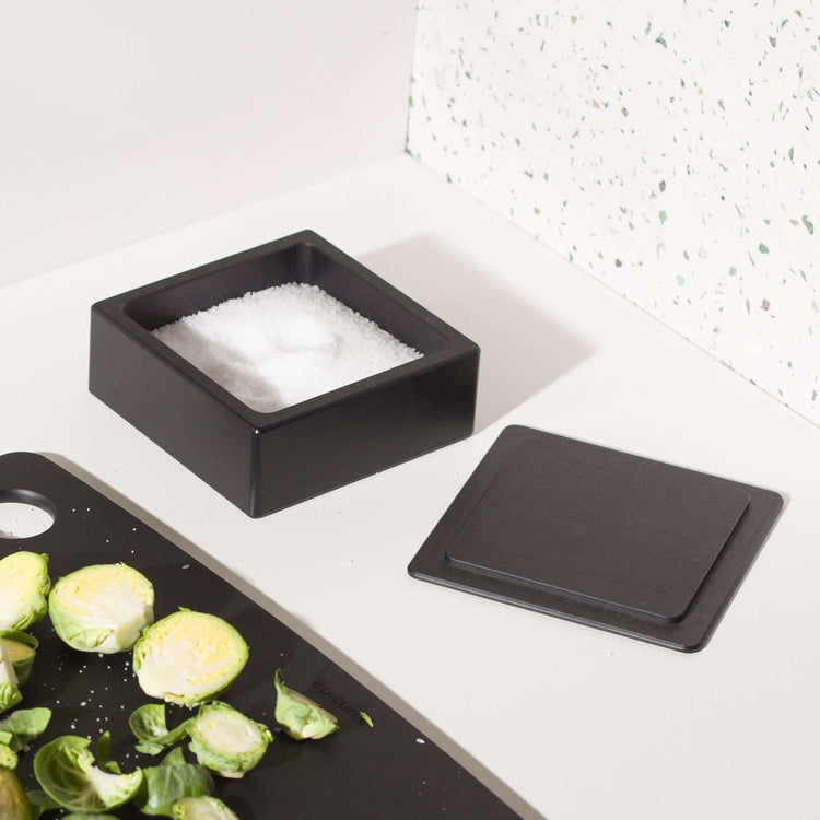 Epicurean Salt Cellar in Slate on a counter filled with salt next to a Slate Epicurean Cutting Board and sliced Brussel Sprouts