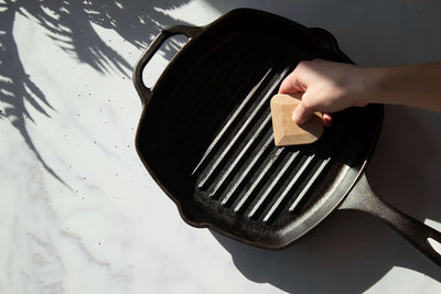 The Natural colored pan scraper being used to clean a cast iron griddle.