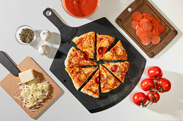 Pizza Peel Plus featured with a cheese and tomato pizza, along side the Handy Series Plus in Natural rectangle with cheese and an All-In-One Cutting Board in Natural with tomatoes 
